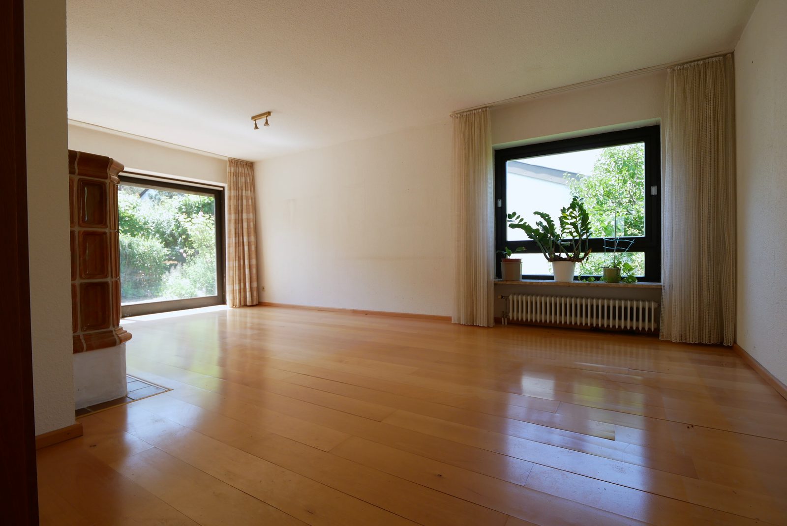 Wohnzimmer vor dem Home Staging: leerer Raum mit Parkett, Kachelofen und Pflanzen am Fenster